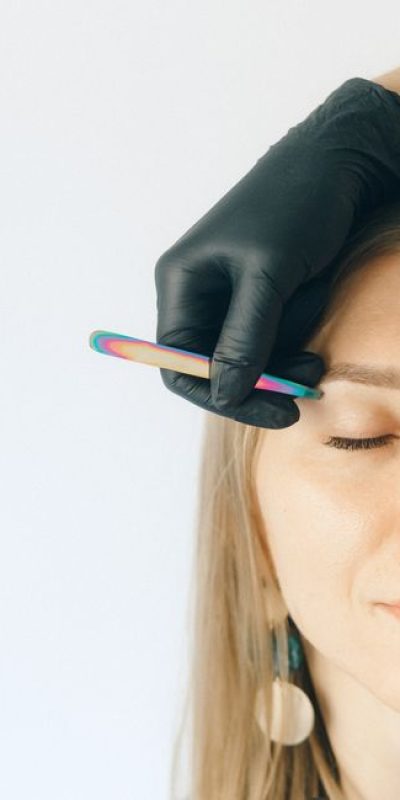 Close-up of a woman receiving an eyebrow plucking treatment with black gloves.